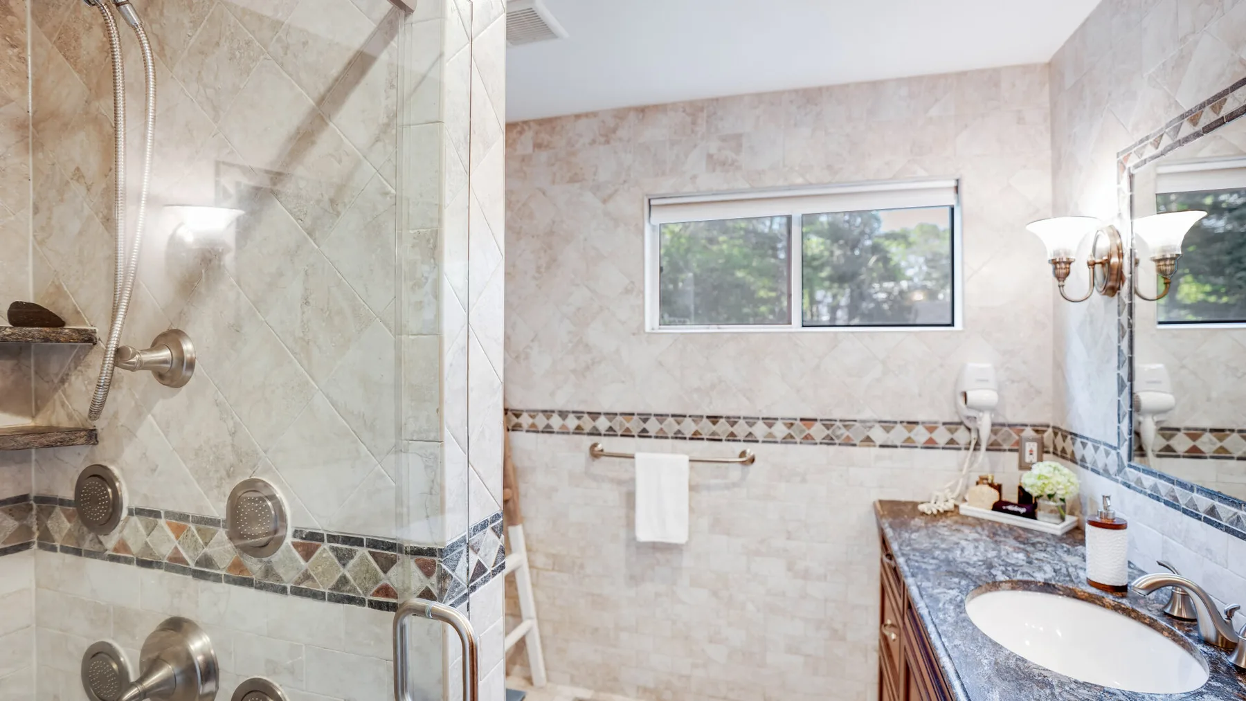 A tiled bathroom features a glass shower, vanity, and window.