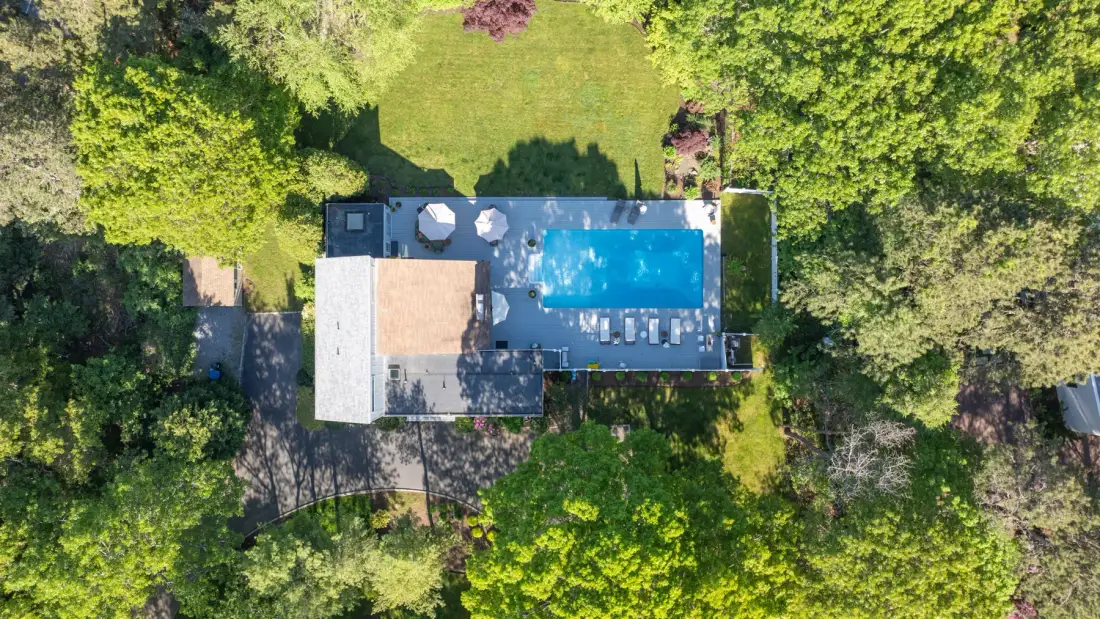 Aerial view of an outdoor pool and paved deck surrounded by trees.