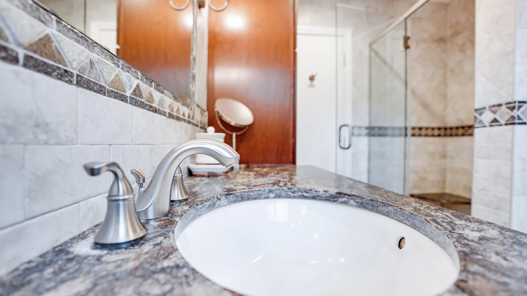A bathroom vanity with an oval sink and a glass shower in the background.
