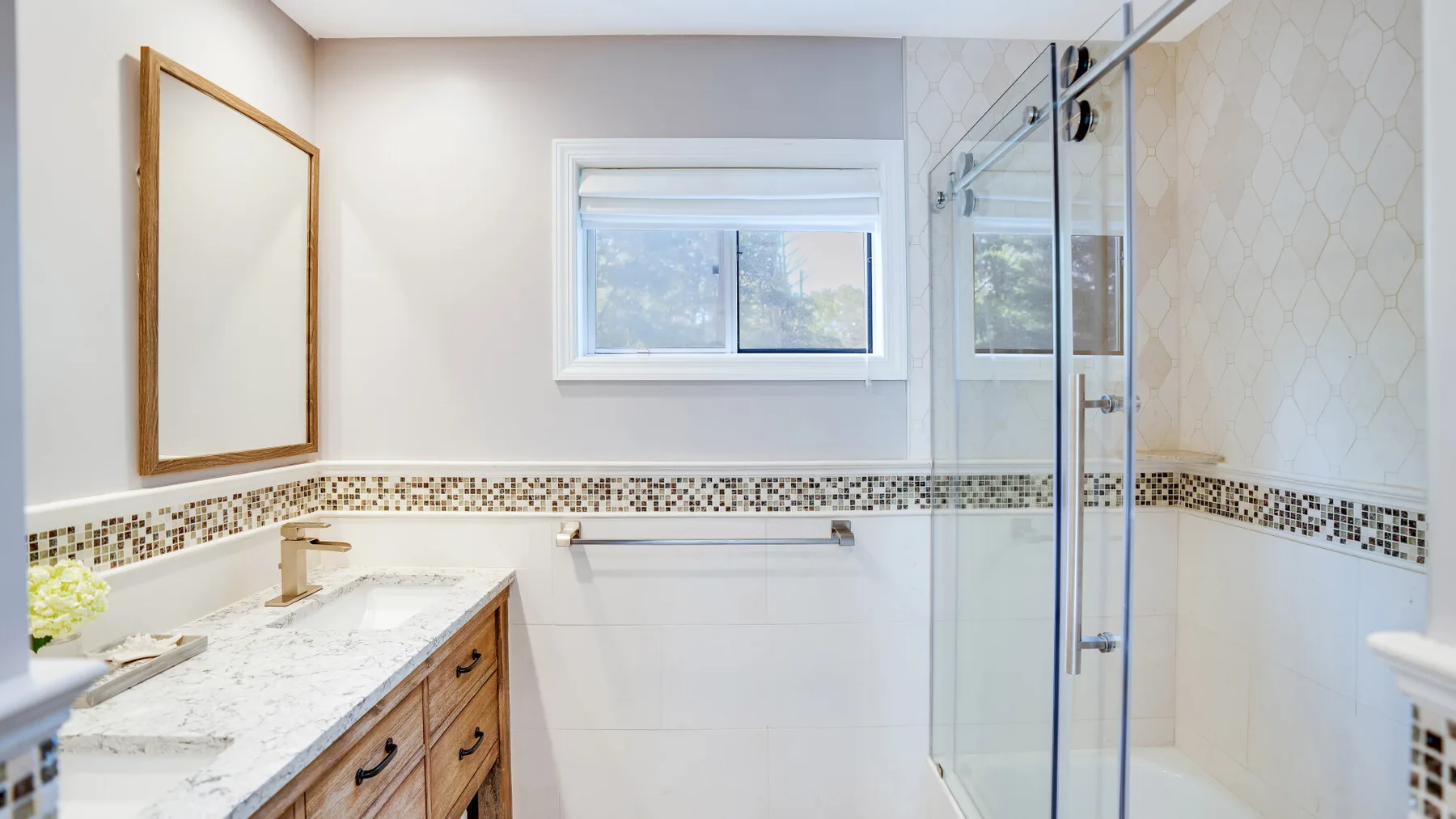 A bright bathroom with a marble vanity, window, and glass shower.