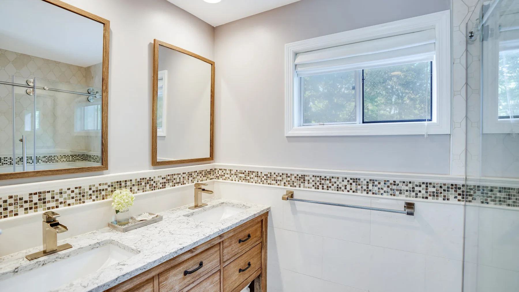 A bright bathroom with a double-sink vanity, mirrors, and a window.