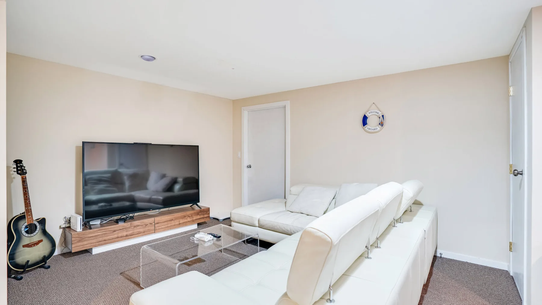 A living room with white seating arranged around a glass coffee table and television.