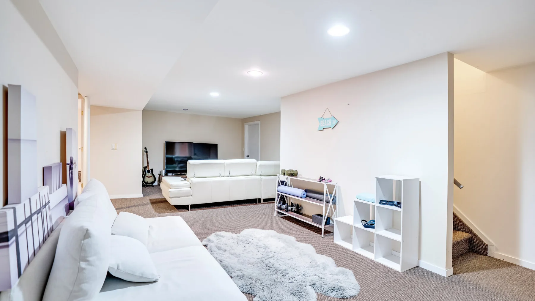 A bright living room with white seating, a television, and a pale rug.