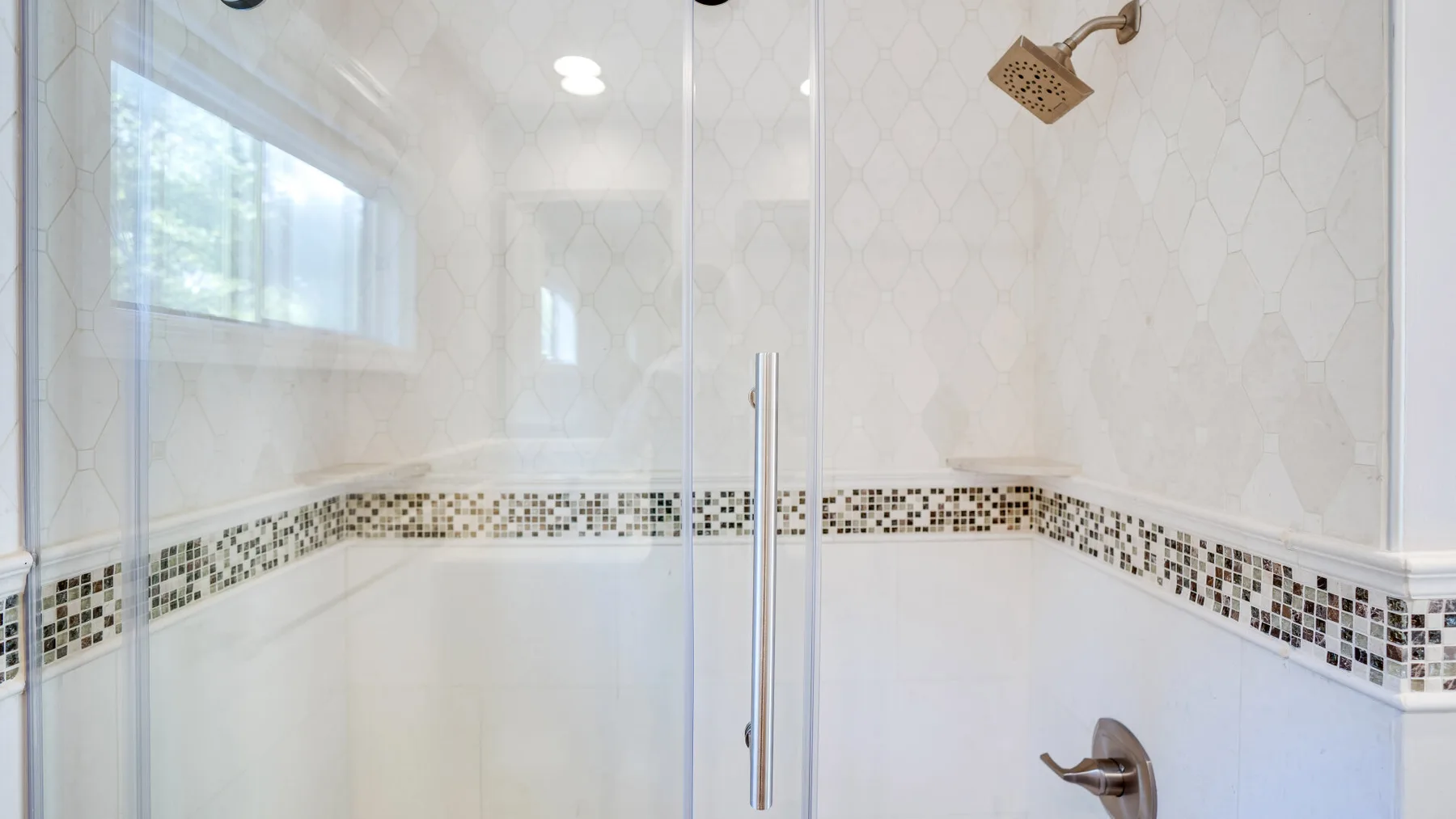 A tiled bathroom shower with glass panels and a patterned tile border.