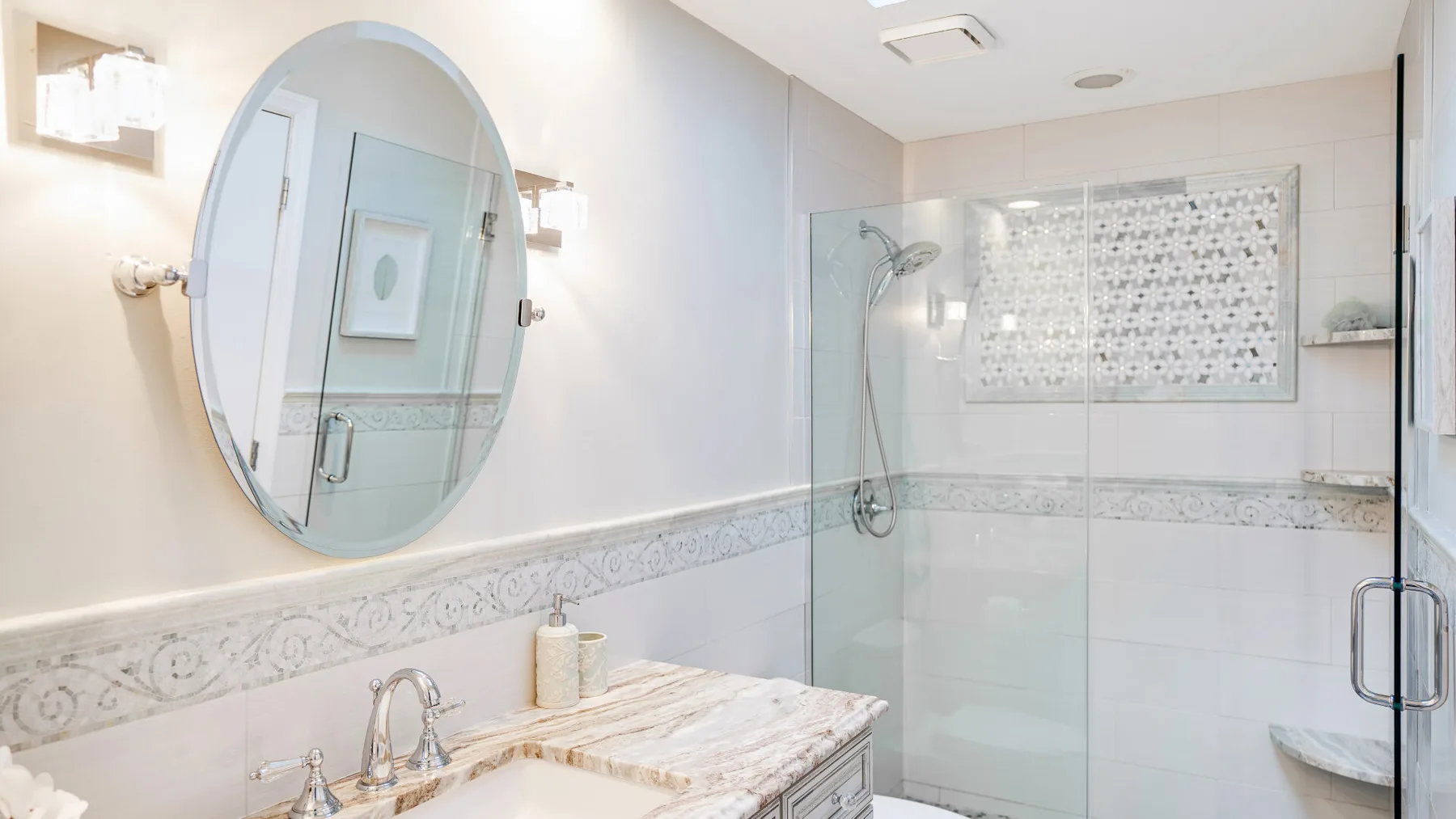 A bright bathroom with a sink, oval mirror, and glass shower.