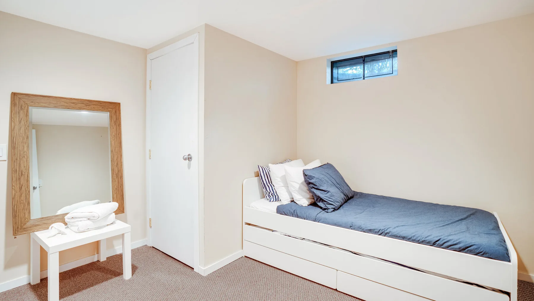 A bedroom with a single bed, a small table, and a wall mirror.