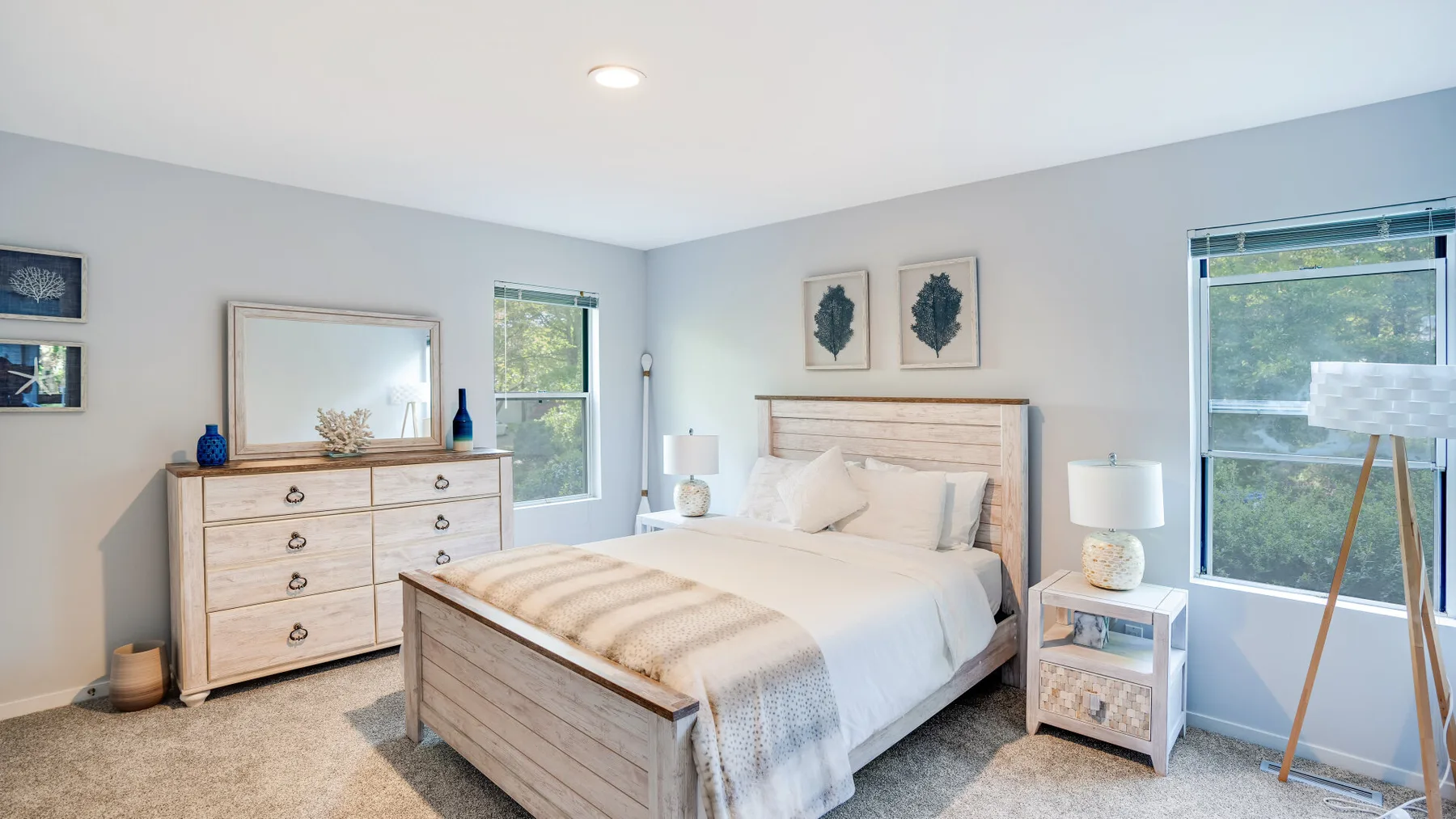 A bright bedroom with a bed between two windows and a dresser.