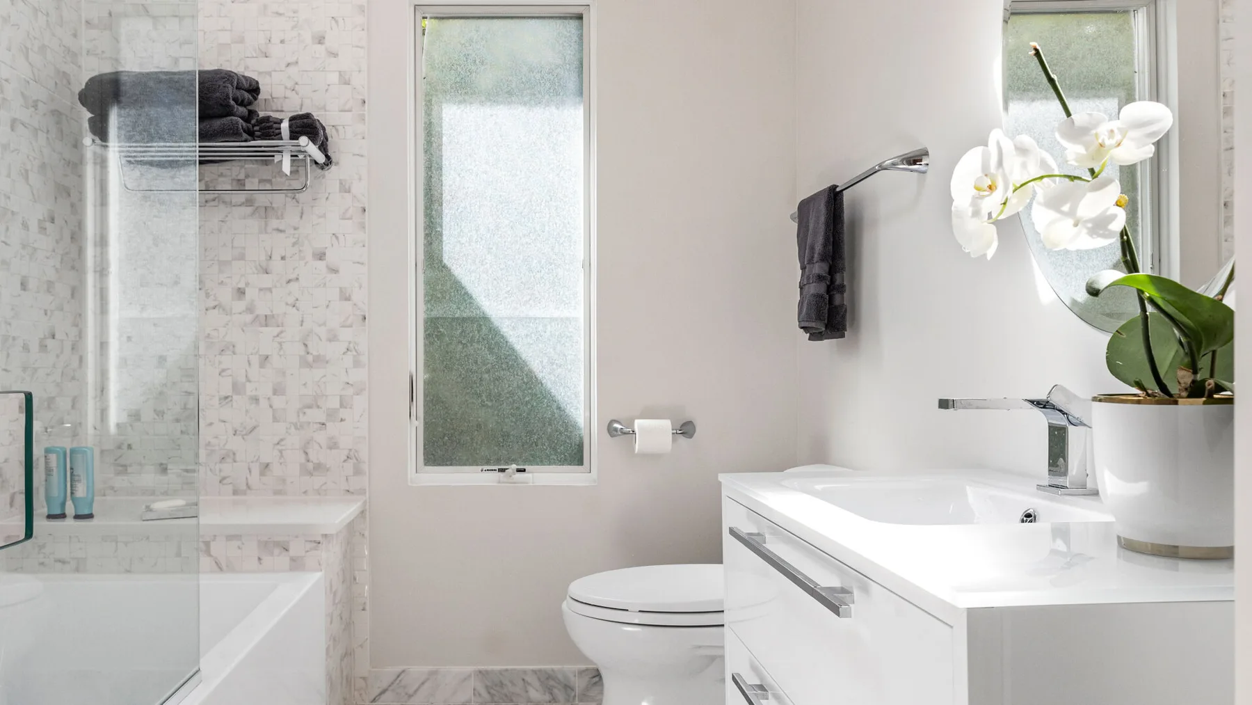 A bright bathroom with a glass shower, bathtub, and white vanity.
