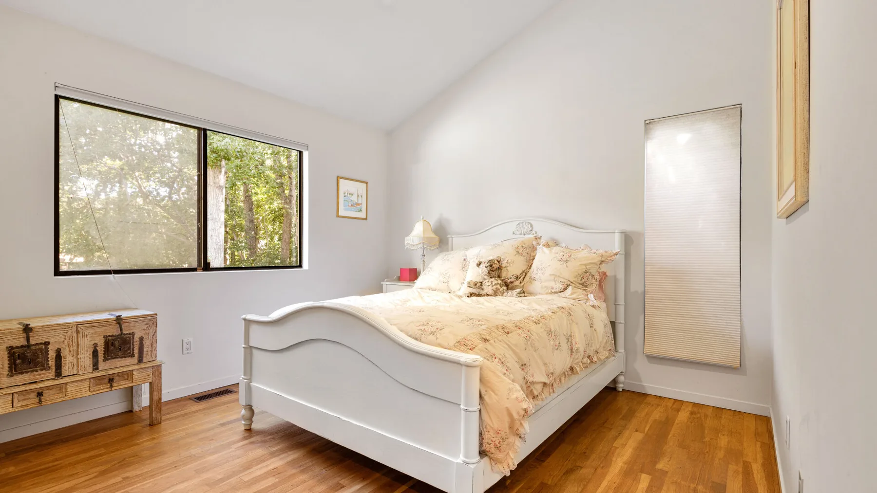 A bedroom with a bed, bedside table, and windows overlooking trees.