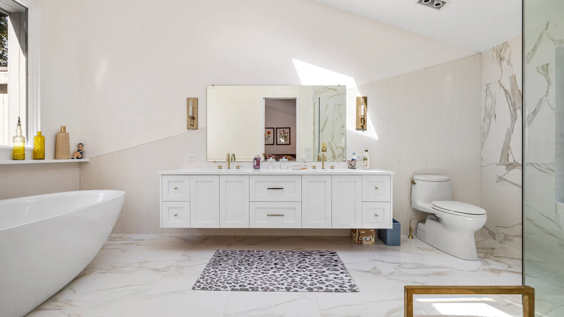 A bright bathroom with a double-sink vanity, bathtub, and toilet.