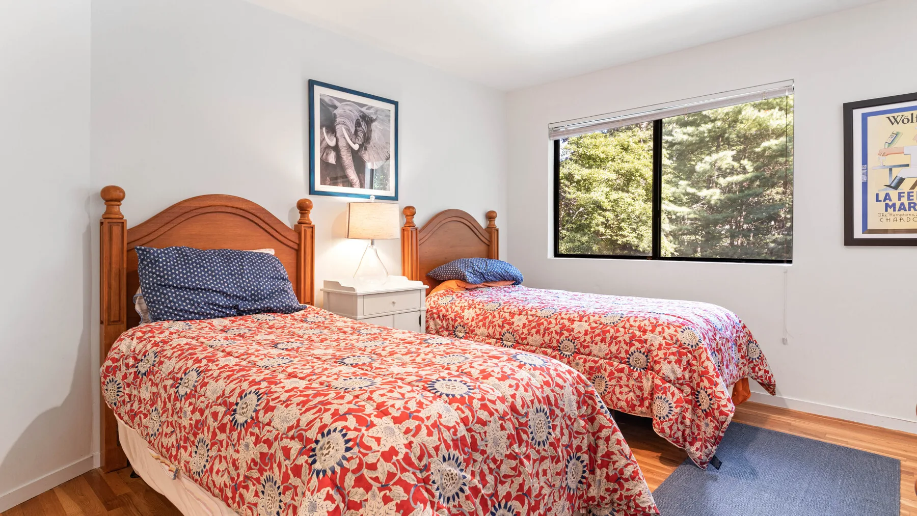A bedroom with two beds covered in red floral bedding beside a window.