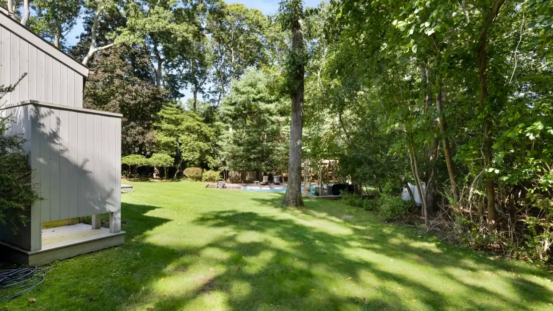 A grassy backyard with mature trees and a small outbuilding.