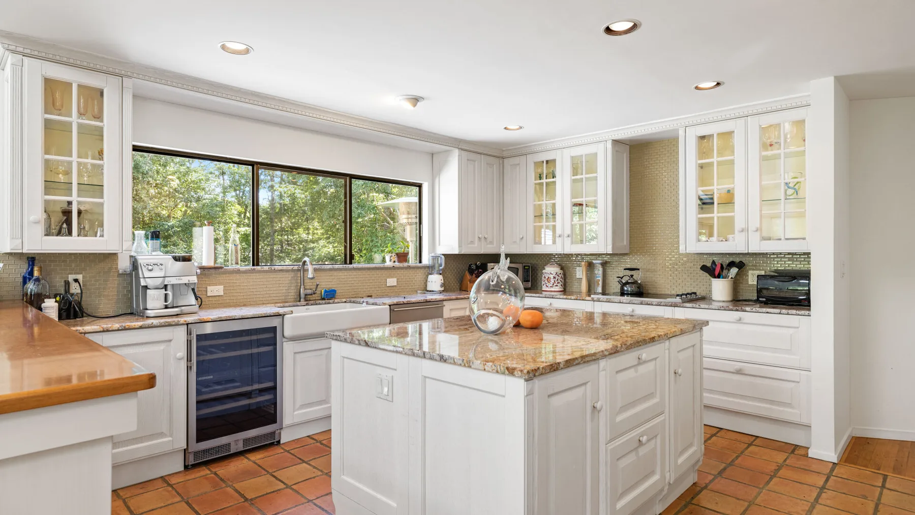 A bright kitchen with white cabinets, a central island, and a large window.