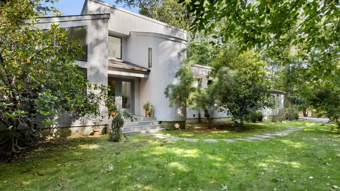 A modern house stands beside a leafy garden and green lawn.