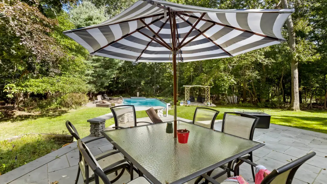 A shaded outdoor dining area with a table overlooking a swimming pool.