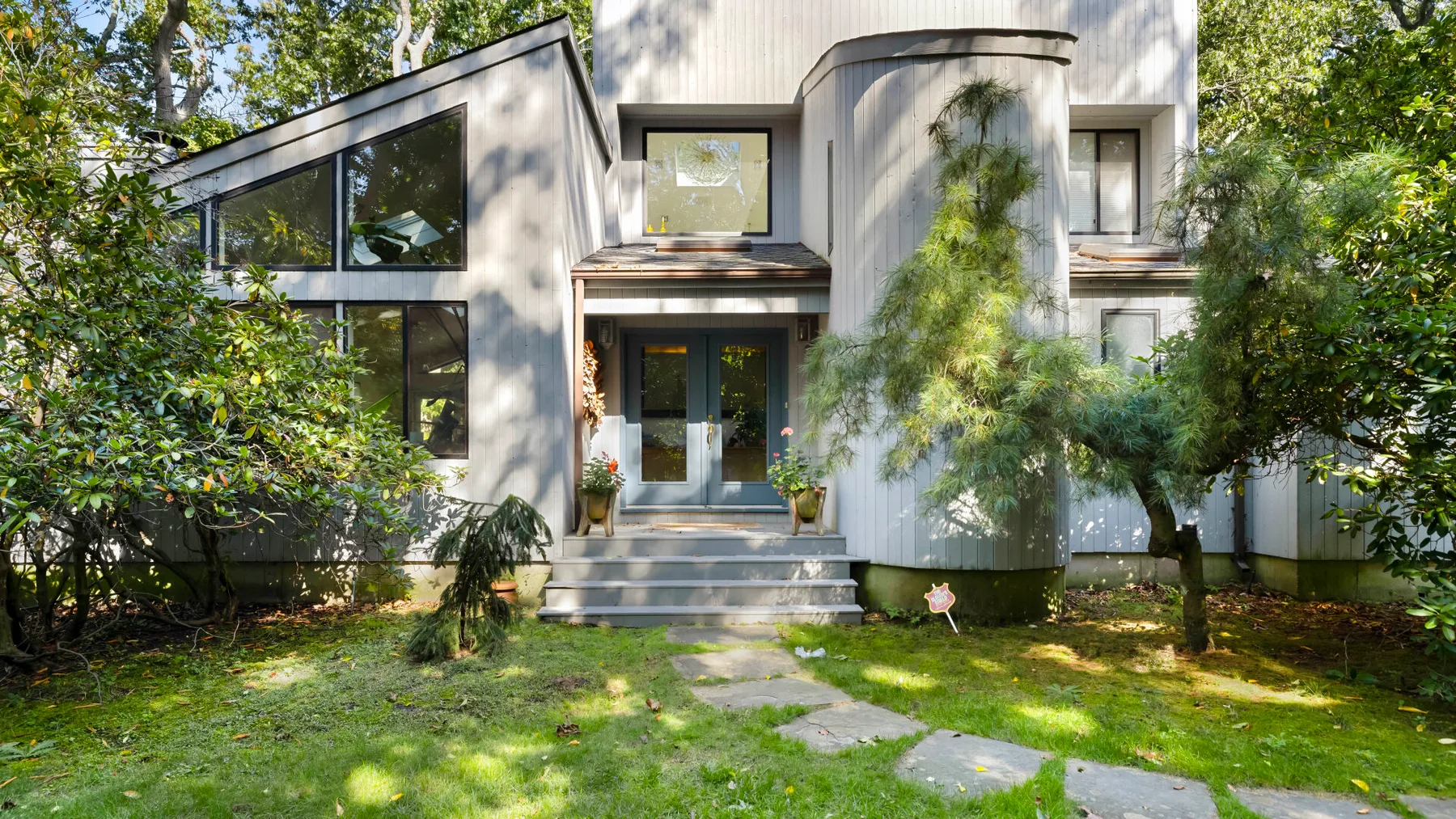 A modern house exterior with a front entrance, windows, and a green garden.