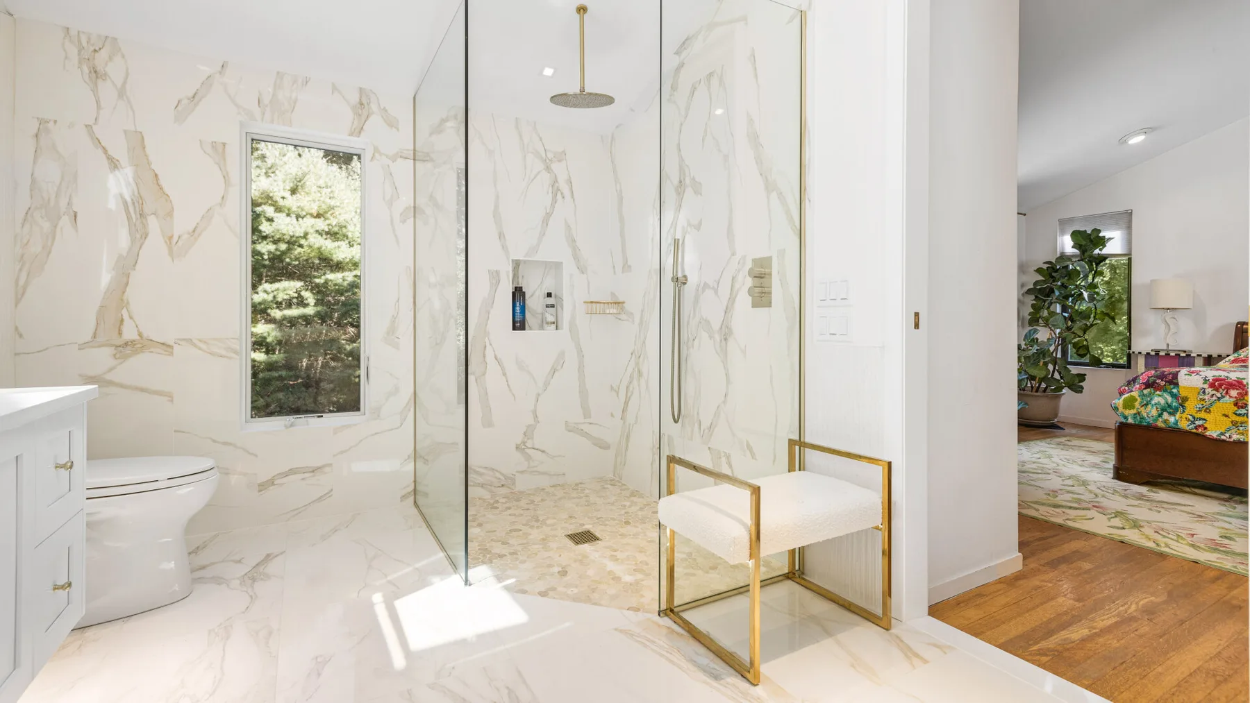 A bright bathroom with a glass shower and a window overlooking greenery.