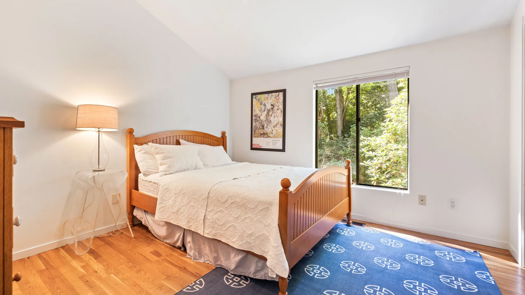 A bright bedroom with a wooden bed beside a large window.