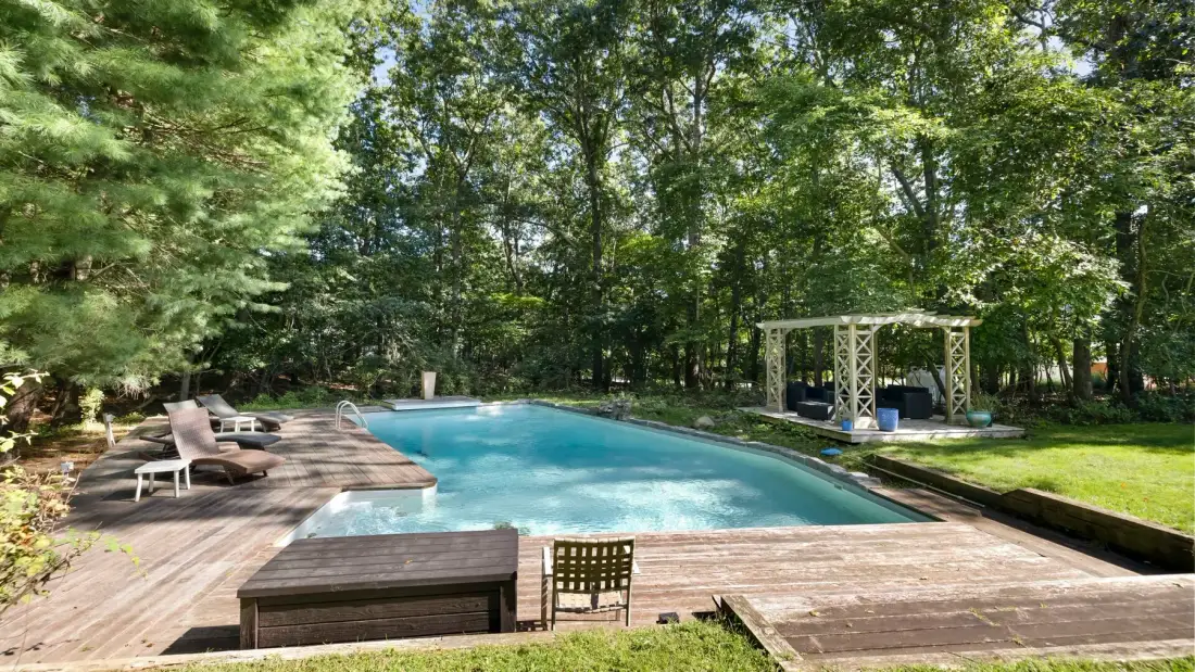 An outdoor swimming pool is surrounded by a wooden deck and trees.