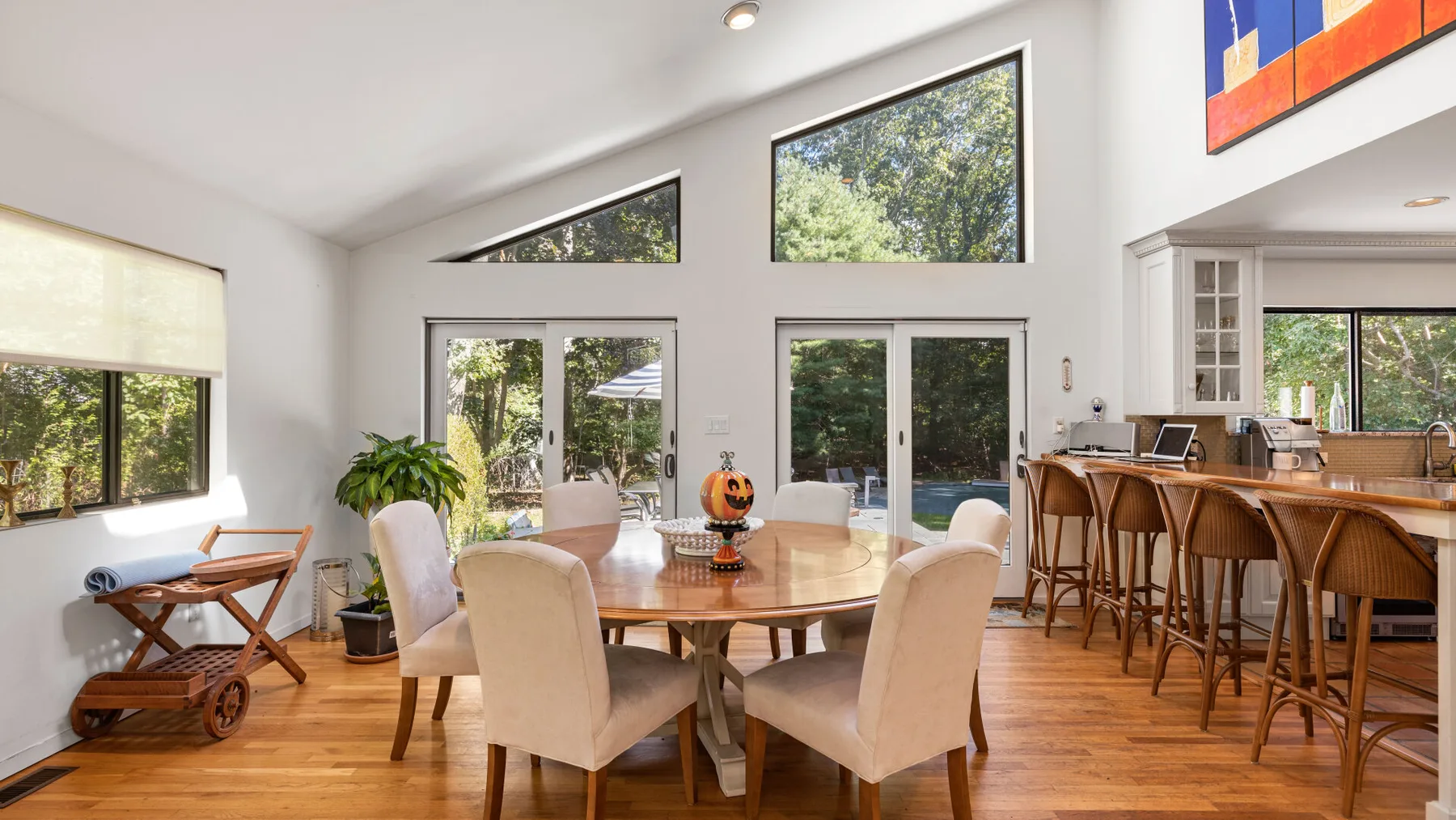 A bright dining area with a round table, large windows, and an adjoining kitchen.
