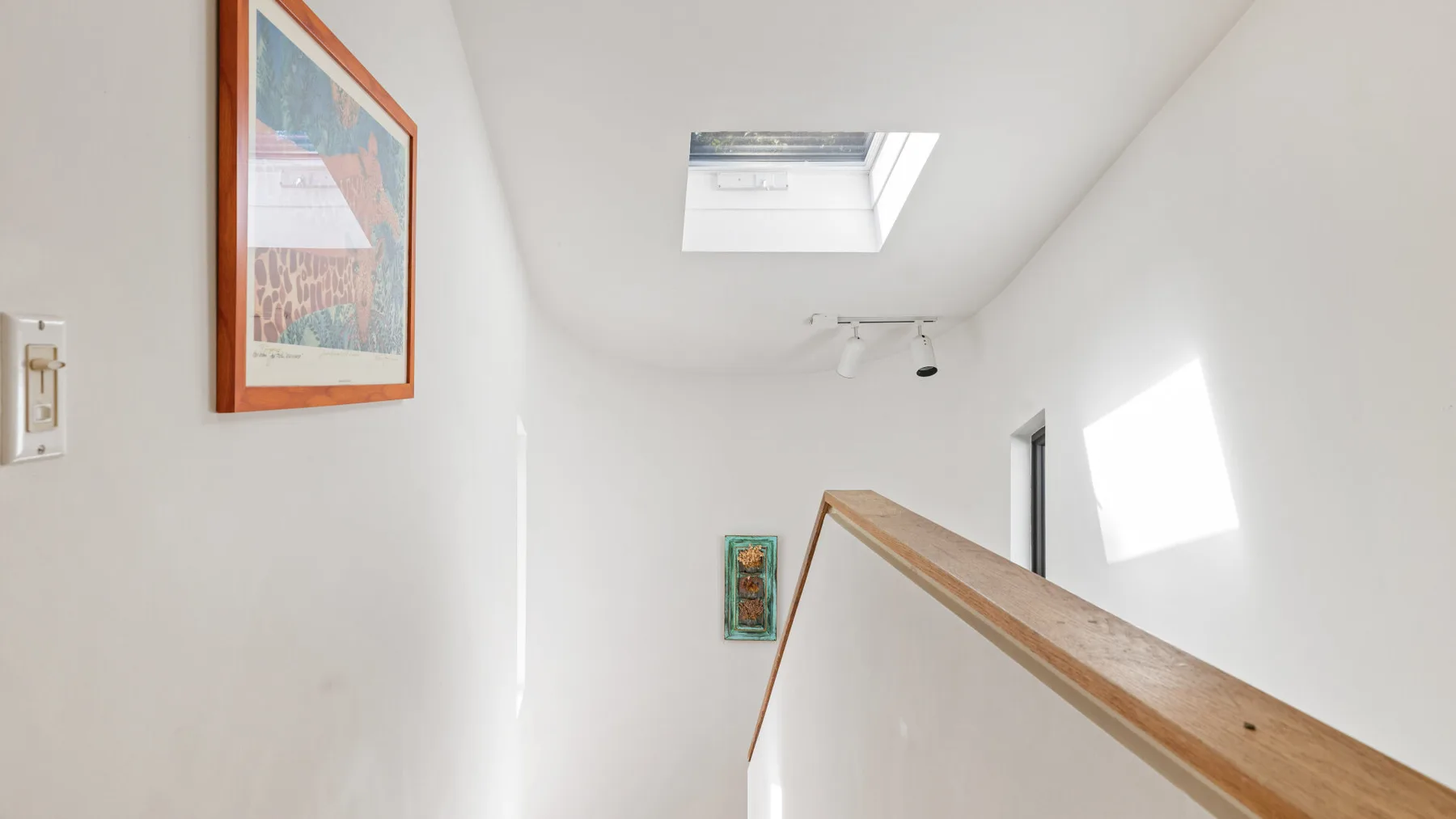 A bright stairwell with a wooden handrail and a skylight.