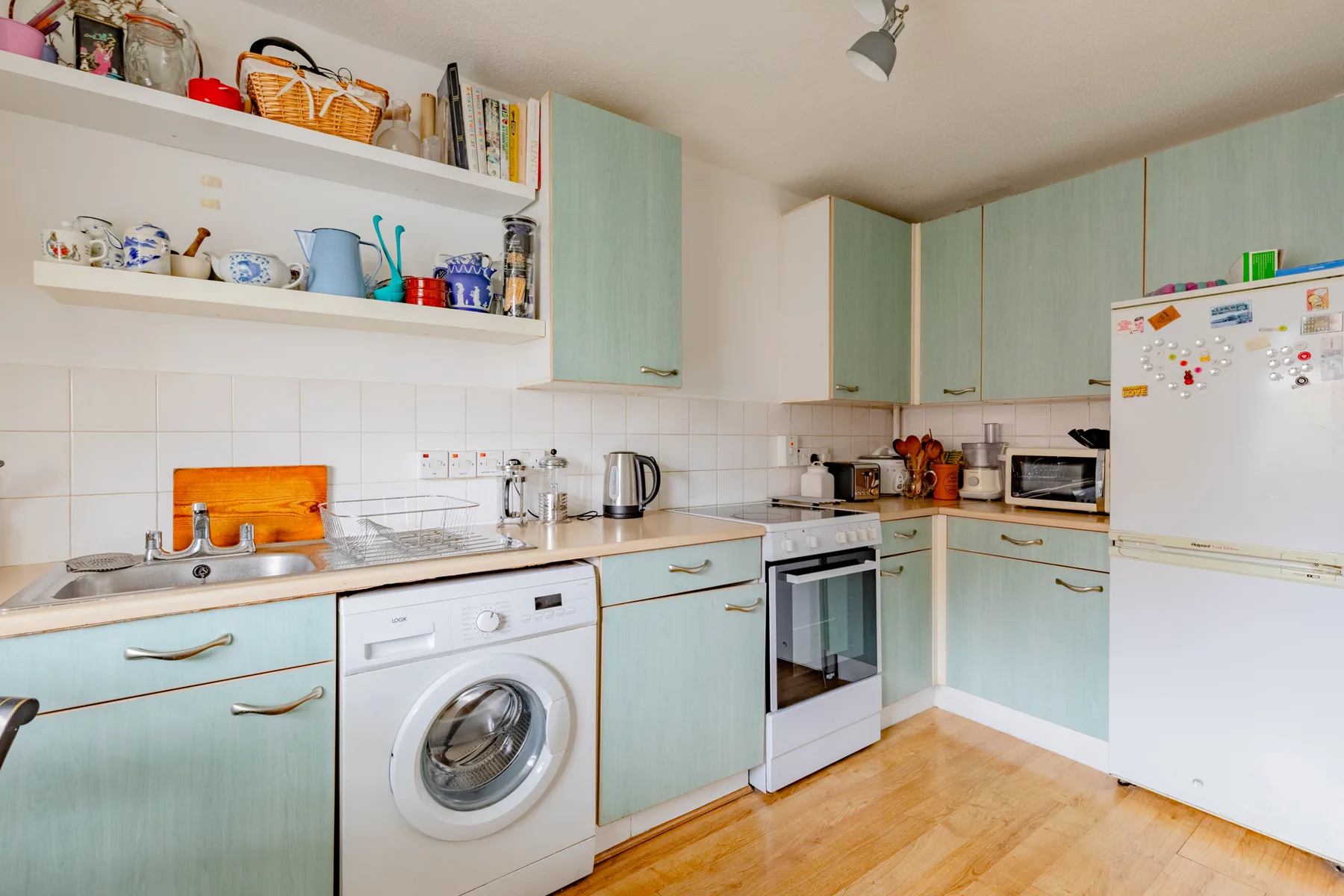 Una cocina luminosa con armarios verde claro, una lavadora y un refrigerador.