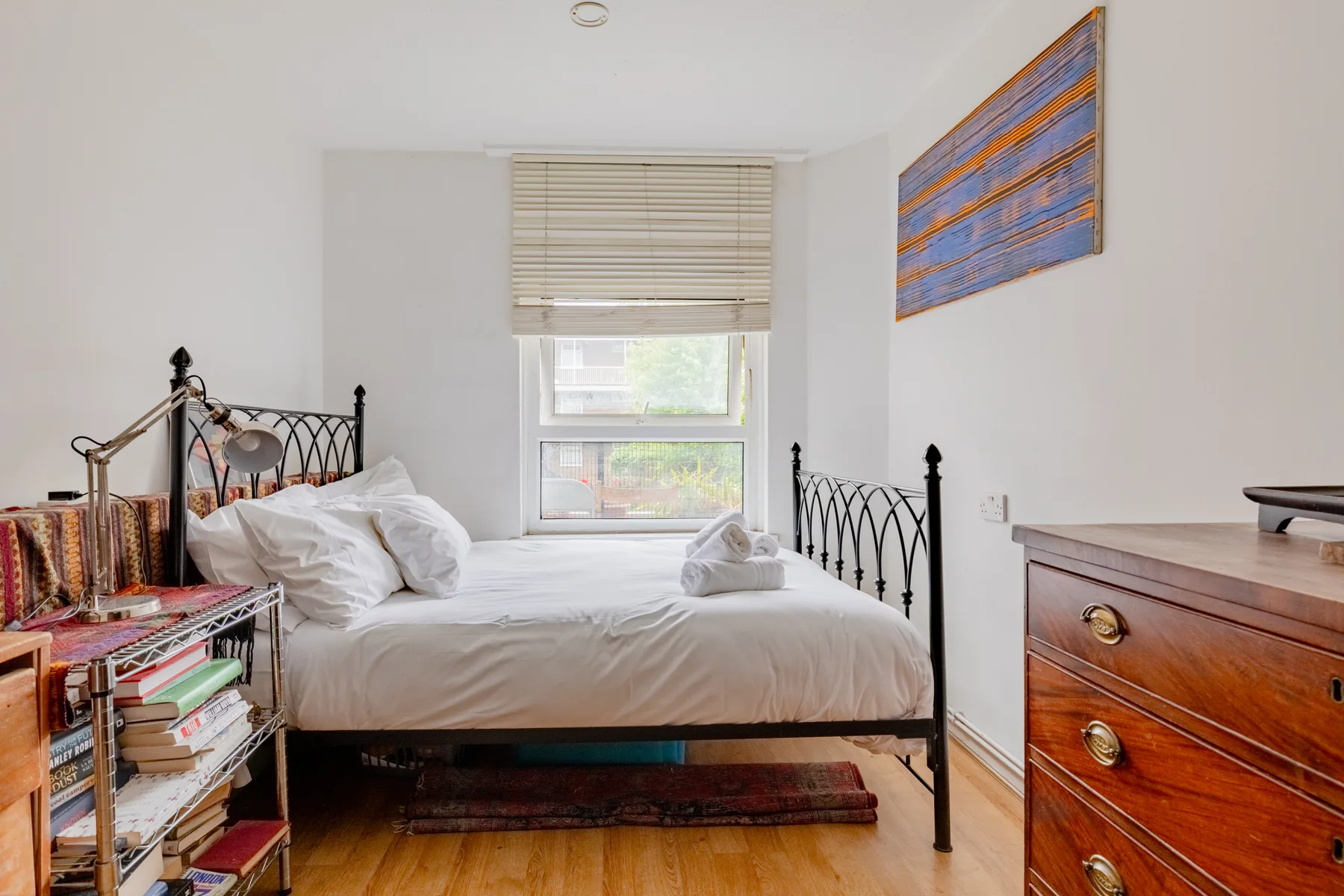 Un dormitorio con una cama bajo una ventana y una cómoda de madera.