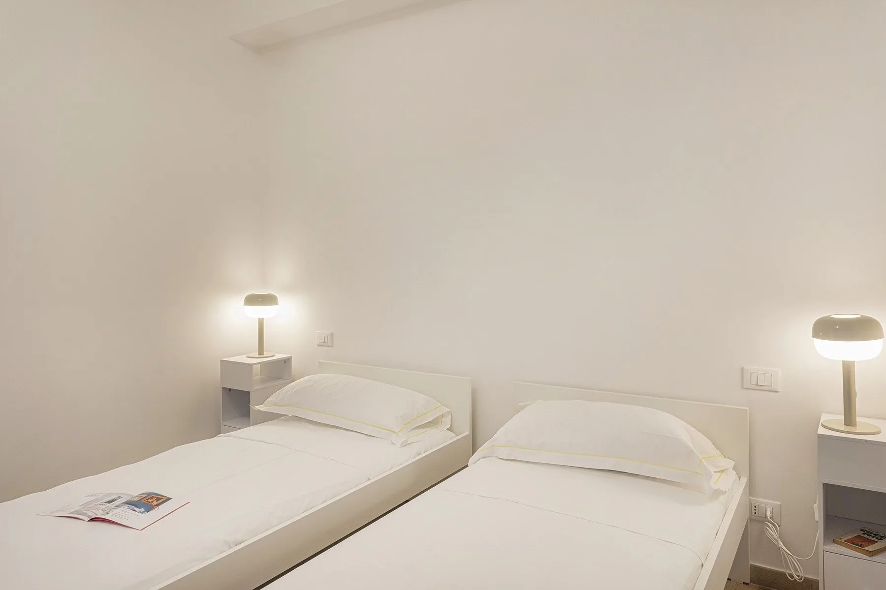A bright bedroom with two beds and bedside lamps.