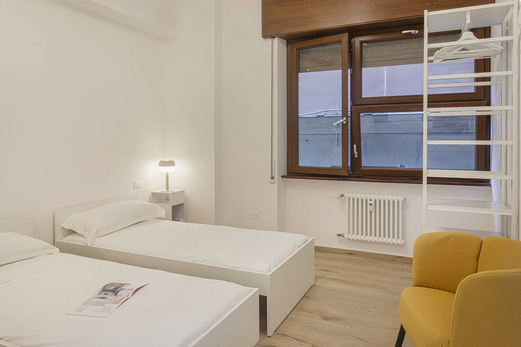 A bedroom with two beds, a bedside lamp, and a window.