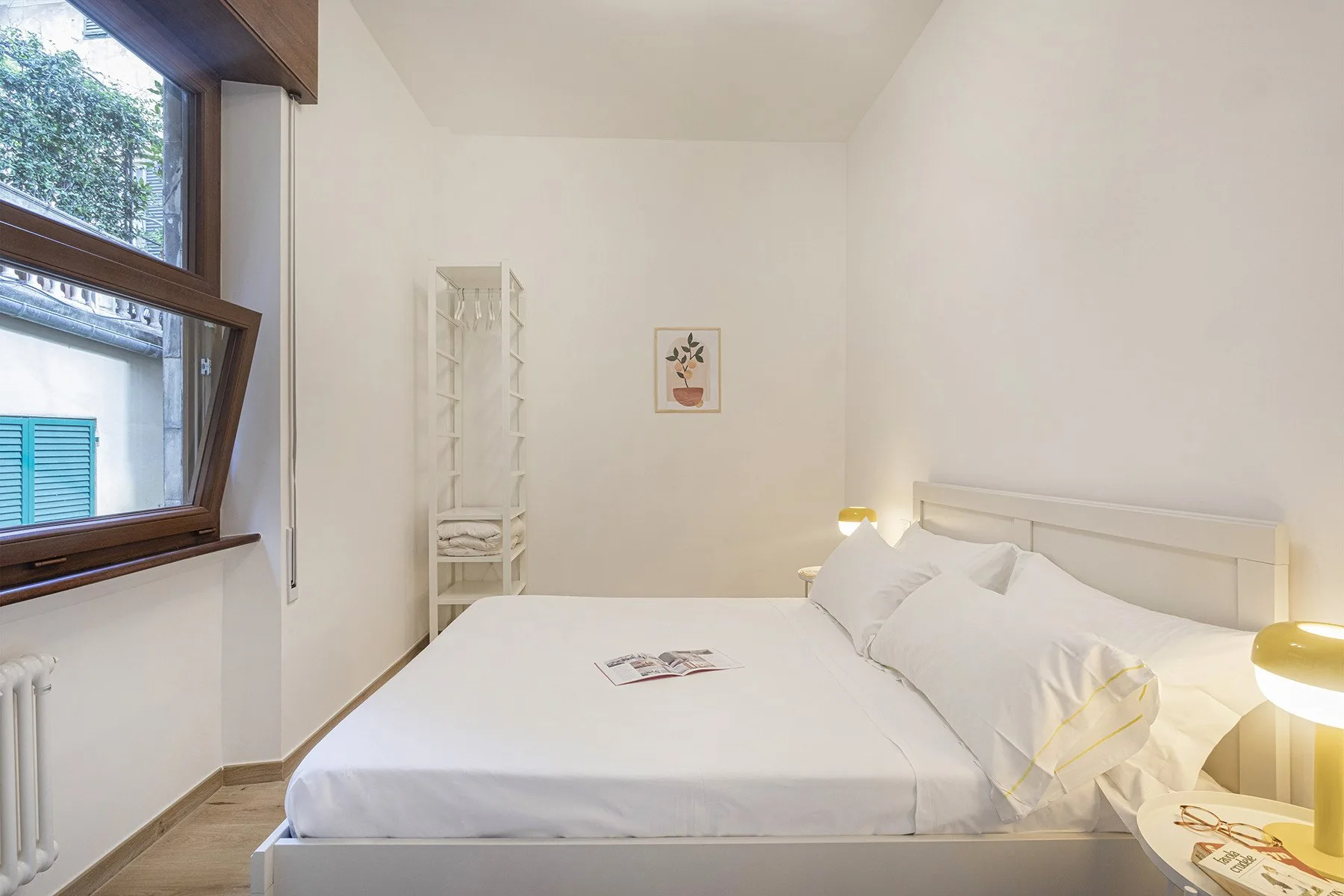 A bright bedroom with a bed beside a large window.