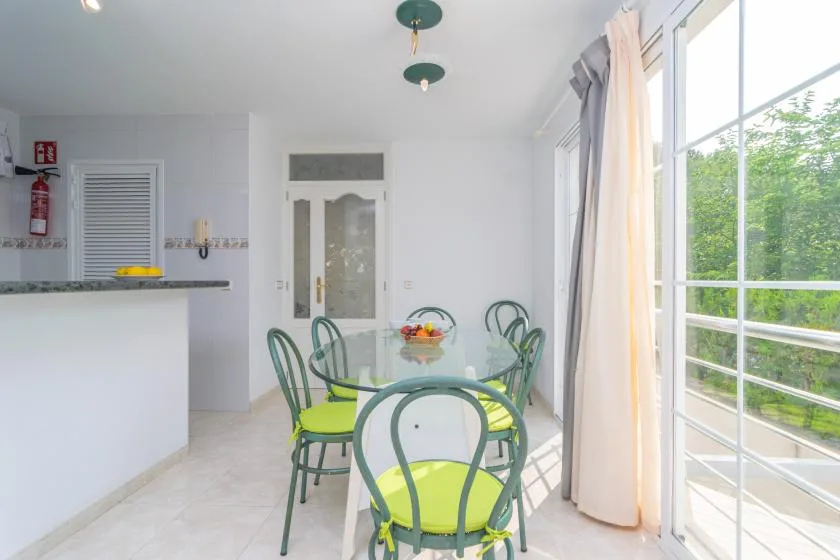 Un comedor luminoso con asientos verdes junto a grandes ventanas.