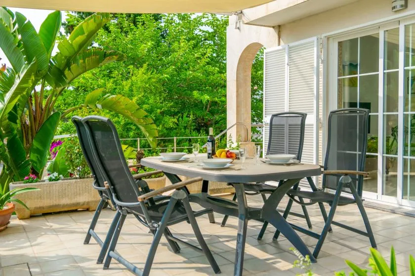 A shaded patio dining area with a table and chairs beside sliding glass doors.