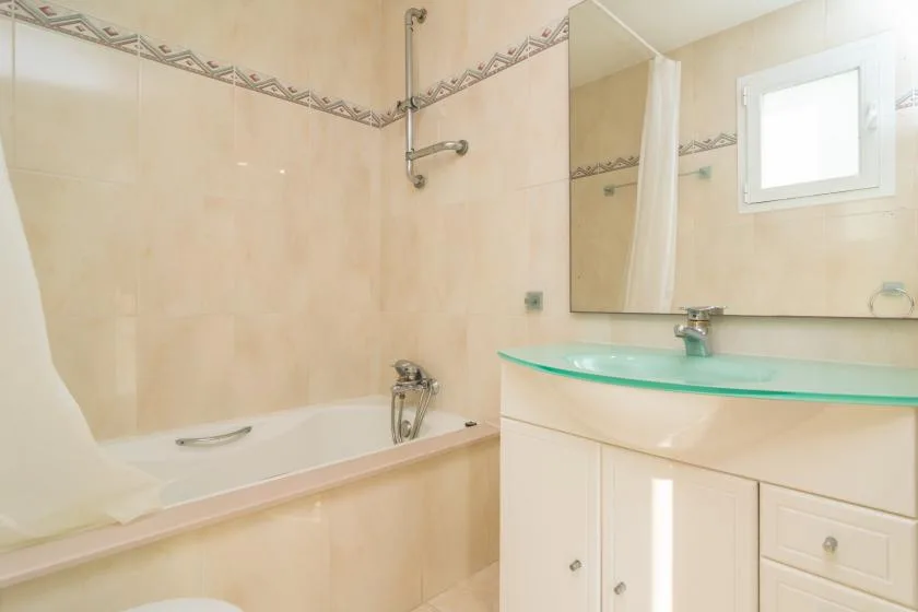 Un baño con bañera, grifo de ducha y lavabo bajo un espejo.