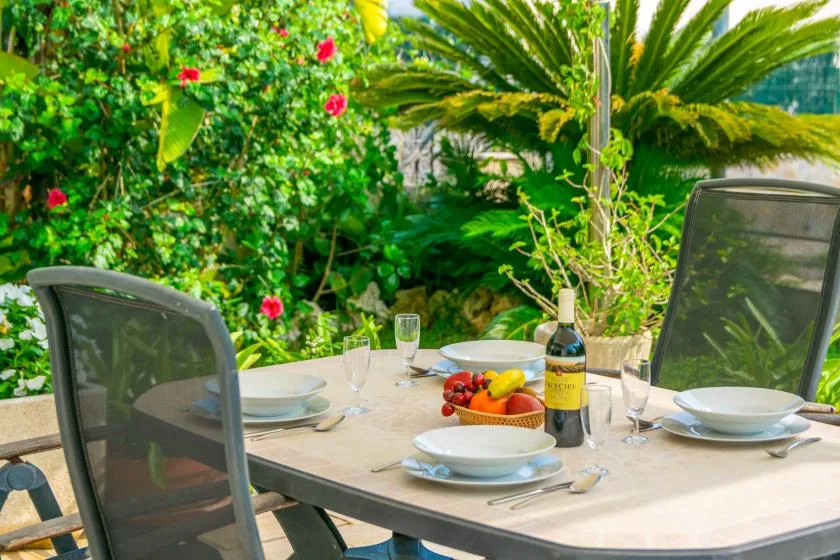 Una mesa de comedor al aire libre está puesta con platos y rodeada de vegetación frondosa.