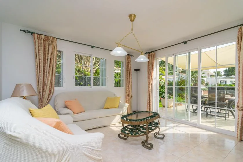 A bright living room with seating and large windows opening onto a garden patio.