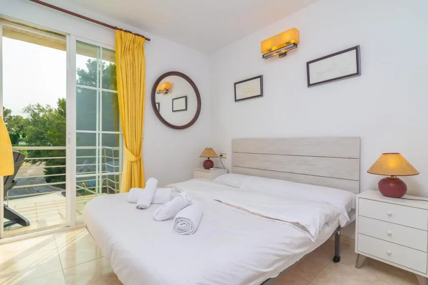 Un dormitorio luminoso con ropa de cama blanca, mesitas de noche y una puerta corrediza de vidrio.