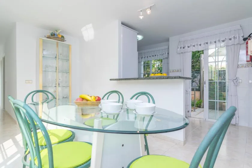 Un comedor luminoso con una mesa de vidrio y asientos verdes.