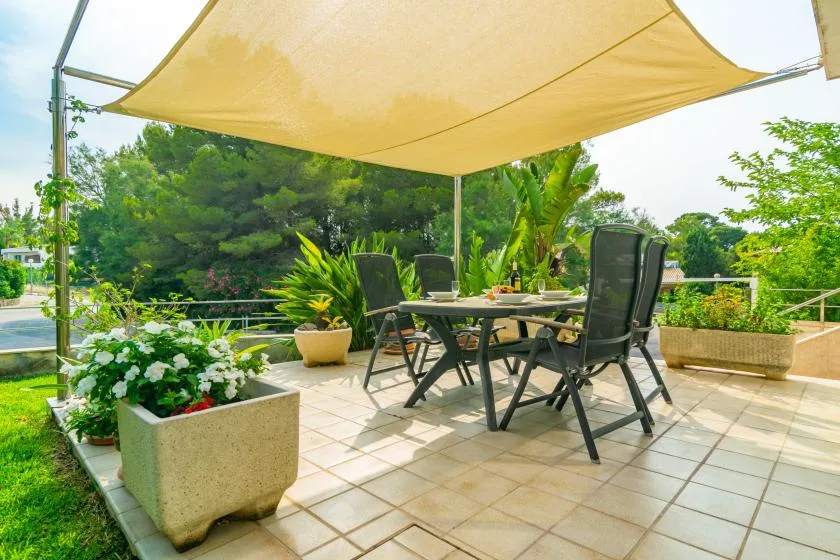 An outdoor dining terrace shaded by a canopy, with a table and chairs.