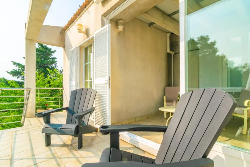 Una terraza exterior con suelo de baldosas tiene asientos junto a grandes puertas de vidrio.