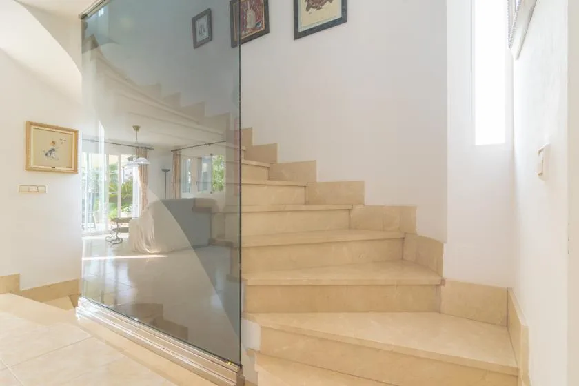 Una escalera interior luminosa con peldaños claros y una barandilla de vidrio.