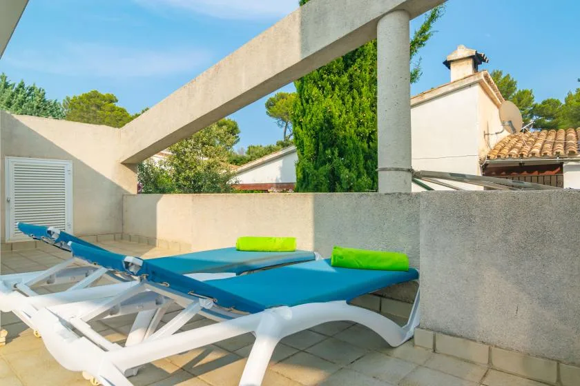 Una terraza al aire libre tiene asientos azules, estructuras blancas y un muro bajo de hormigón.