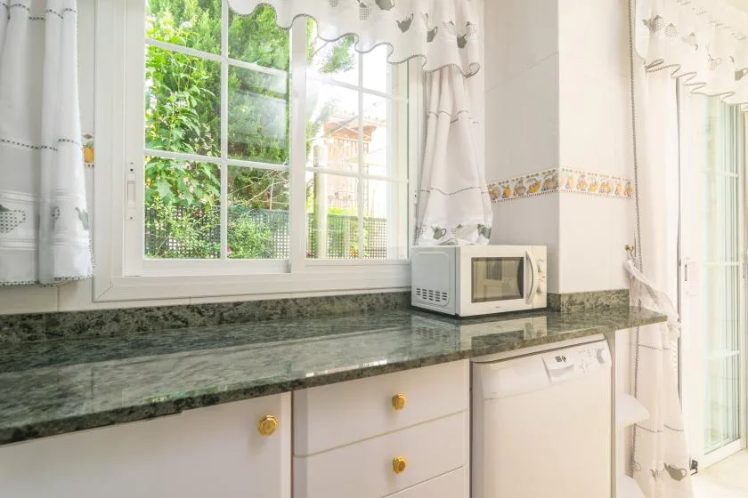 Una cocina luminosa con encimera, microondas y grandes ventanas.