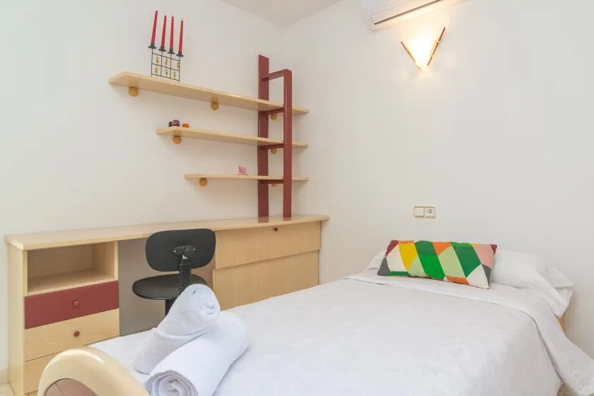 Un dormitorio con una cama bien tendida y estantes en la pared.
