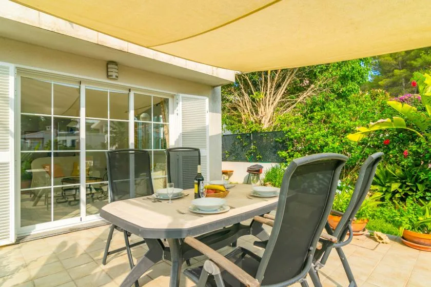Un comedor exterior sombreado con mesa, asientos y vegetación de jardín.