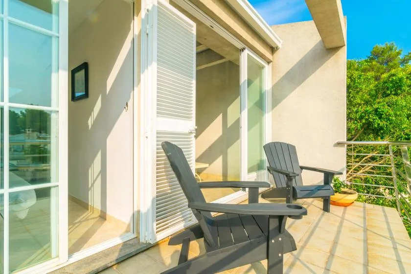Un patio soleado tiene sillas junto a puertas corredizas de vidrio.