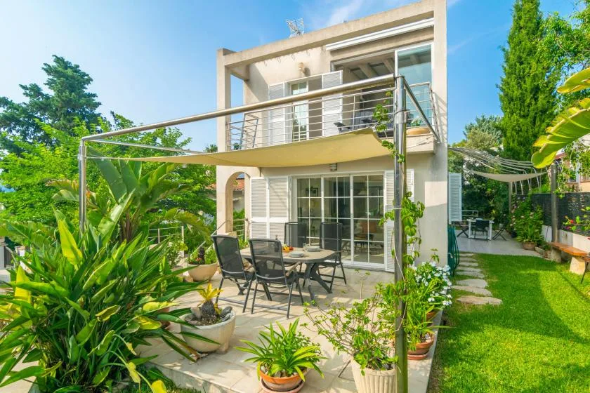Una casa moderna da a un patio ajardinado con asientos al aire libre y plantas frondosas.