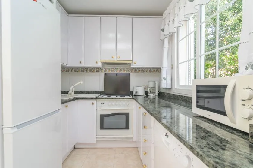Una cocina luminosa con gabinetes blancos, encimeras oscuras y una ventana amplia.