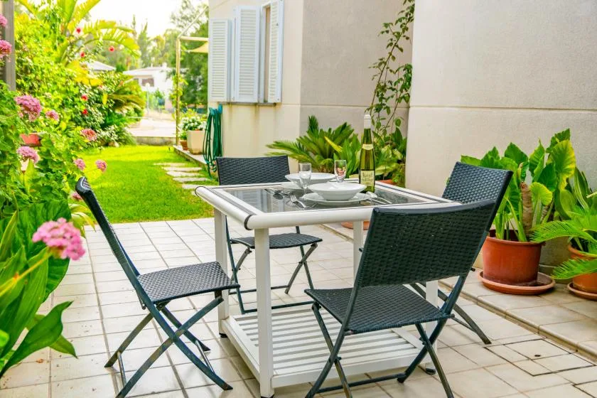 Un patio exterior embaldosado tiene una mesa de comedor y asientos junto a un jardín.
