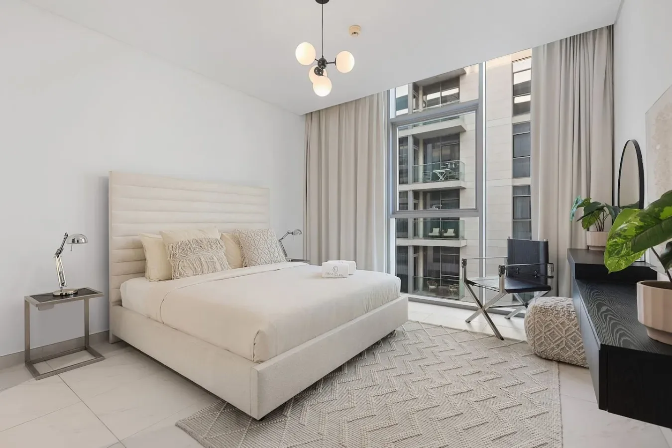 Un dormitorio luminoso con una cama junto a ventanas altas y cortinas claras.