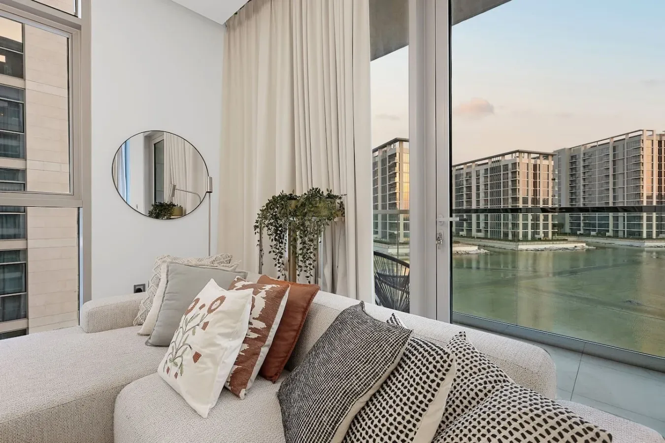 Una sala luminosa con sofá, ventanales de piso a techo y vistas al agua.